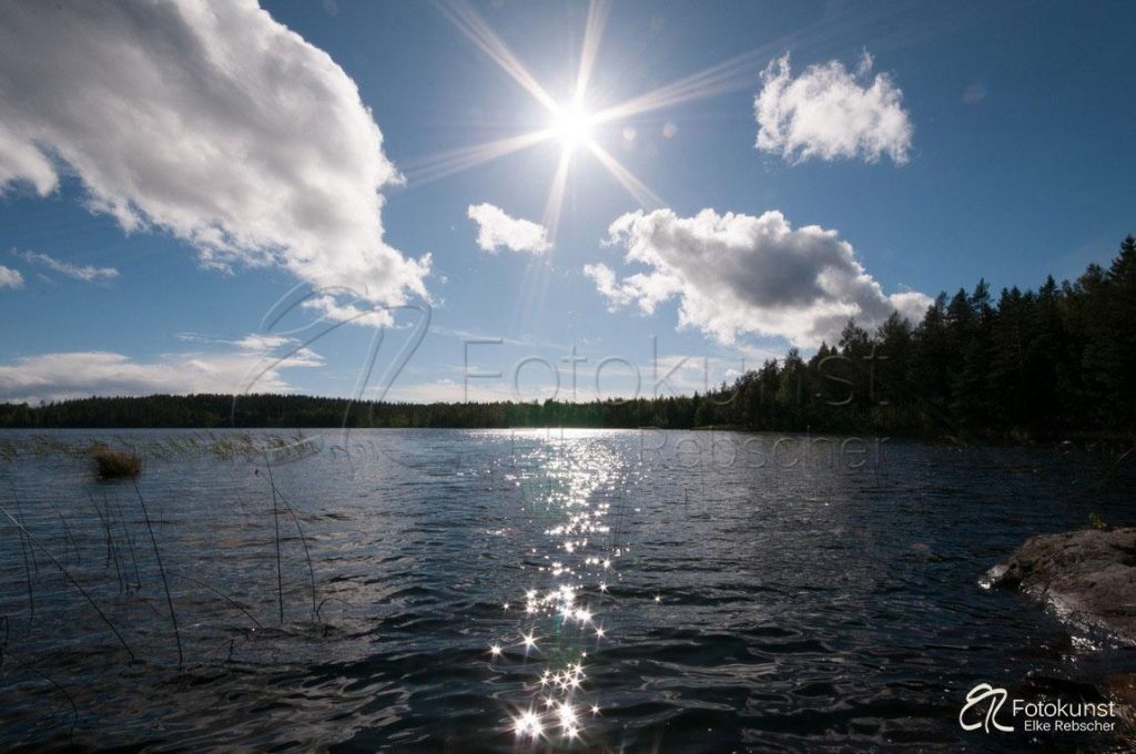 Blick im Gegenlicht über den See Kleven bei Aboda Klint in Südschweden (Smalland) gegen den blauen Himmel und die Sonne, wodurch das Sonnenlicht auf der Wasseroberfläche glitzertt, im